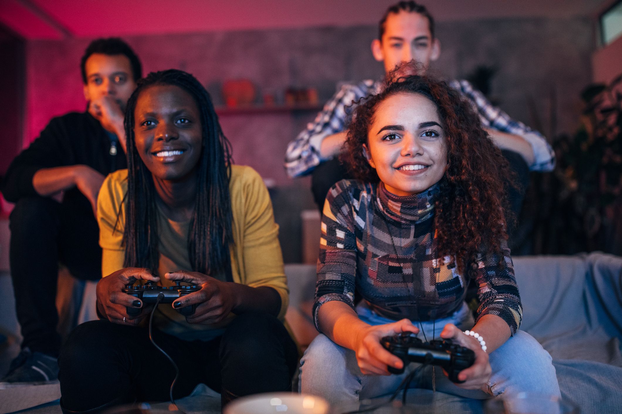 A group of four teenagers play videogames on a couch.