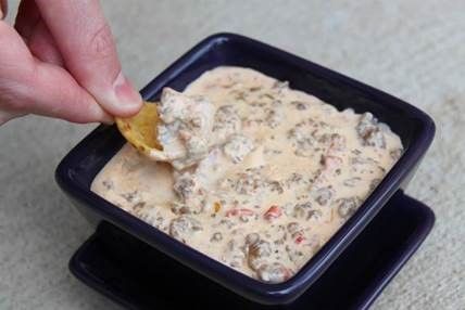 A person extends a chip into a cheesy dip.
