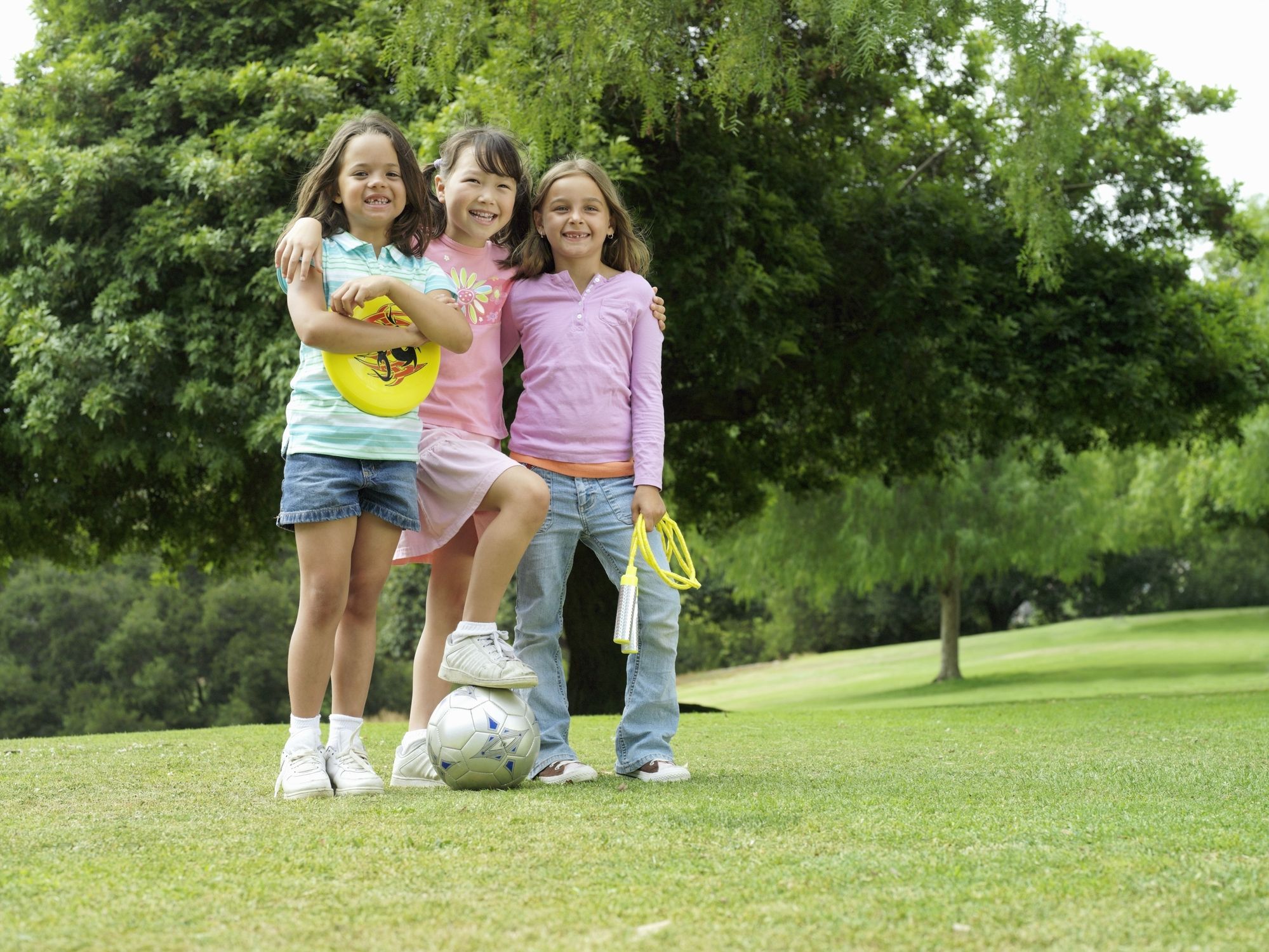 3 young girls pose with a variety of exercise and sports equipment.