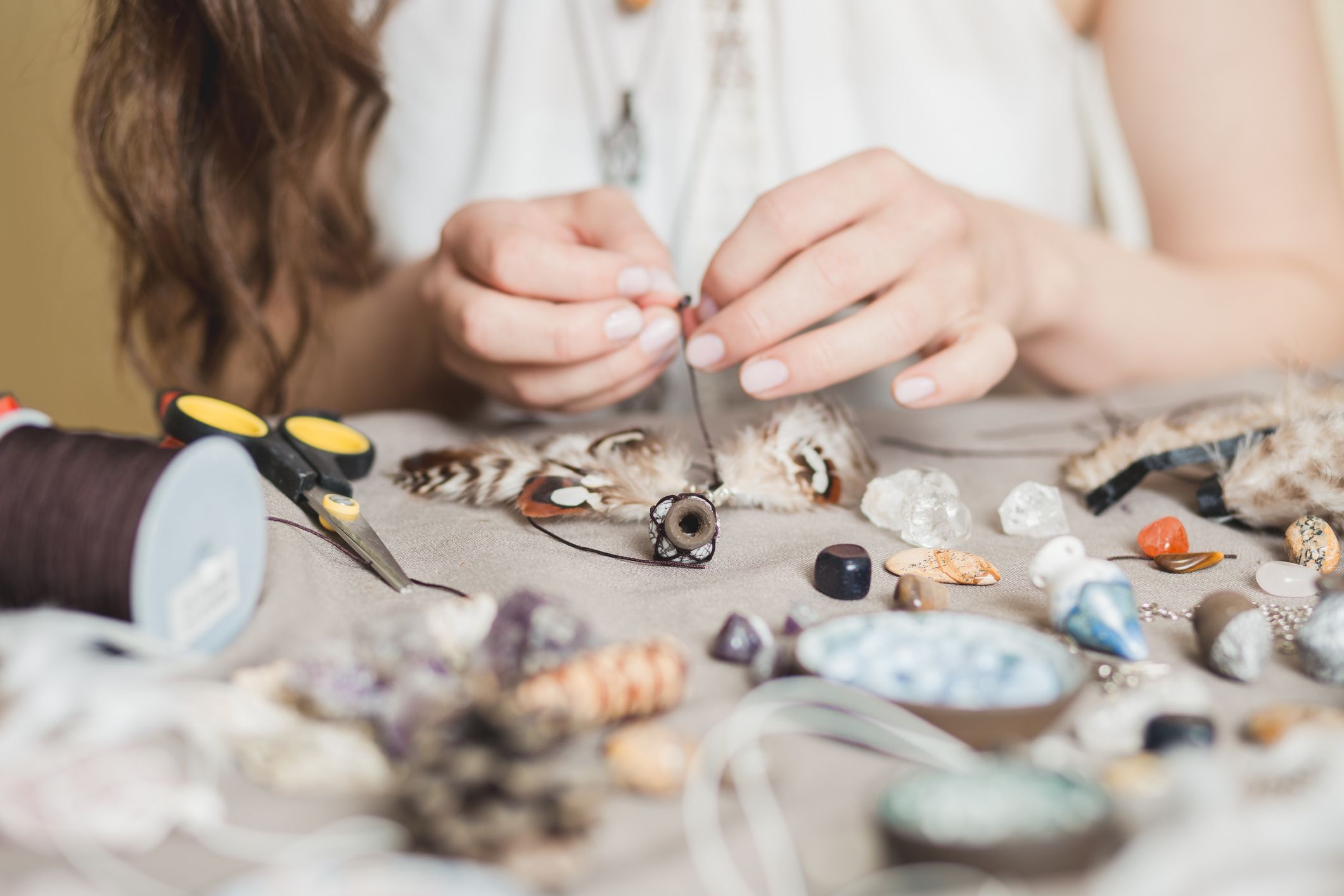 A woman crafts with string, beads, and feathers.