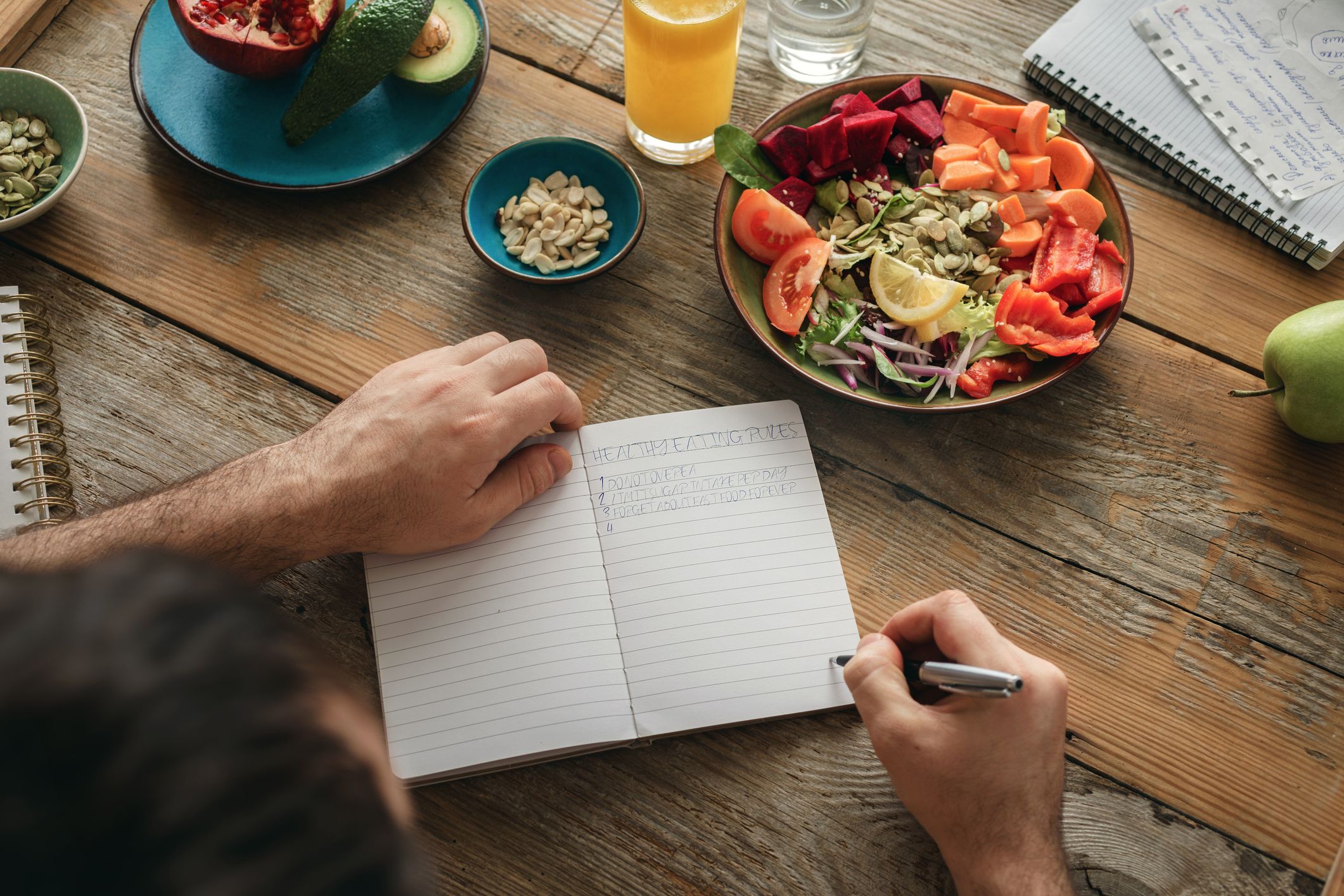 A man journals about &quot;health food rules&quot;, seated at a table filled with fruits and veggies.