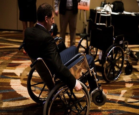 A male in a wheelchair moves across the conference floor.