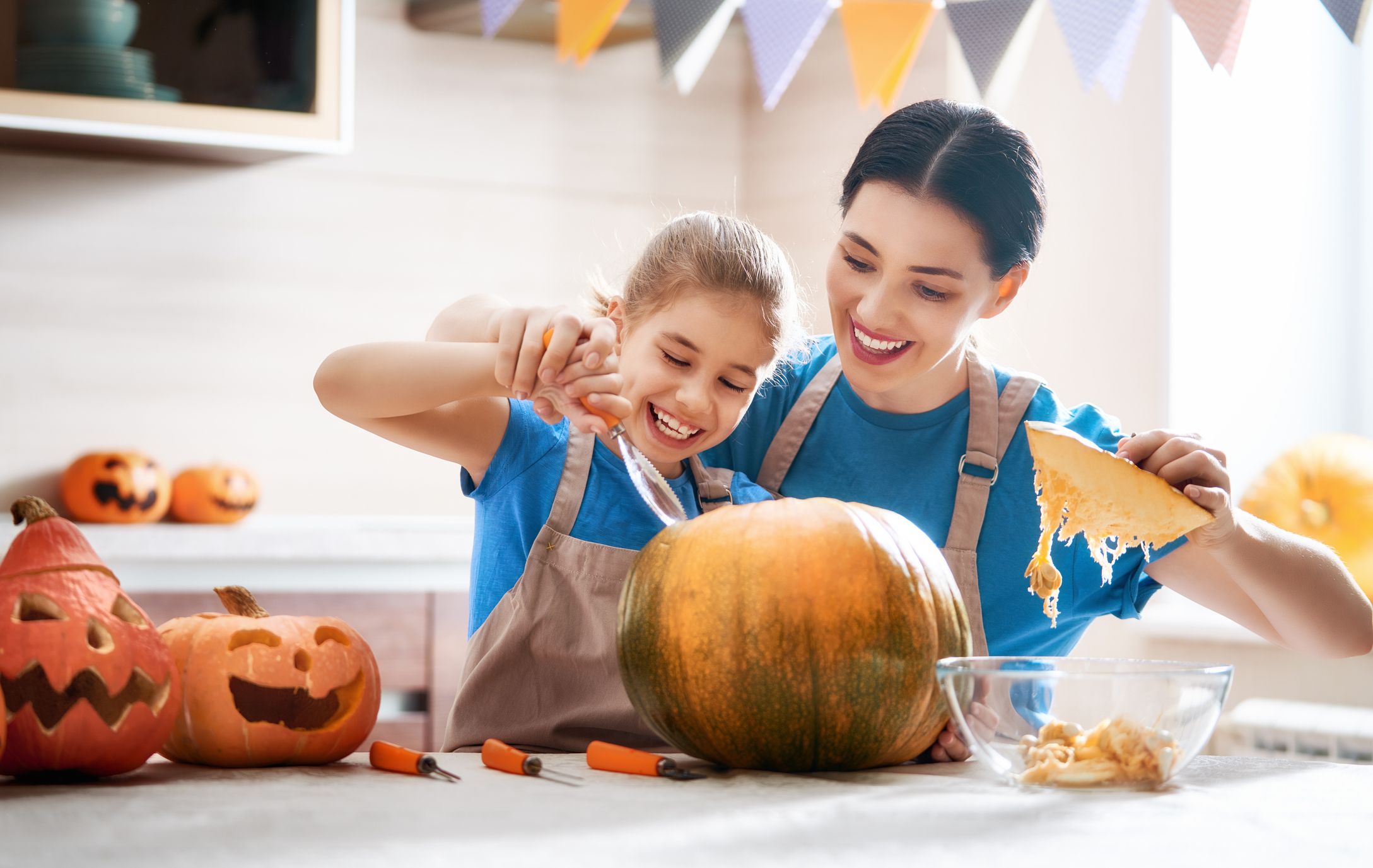 A mother and her young daughter carve a pumpkin in their kitchen.