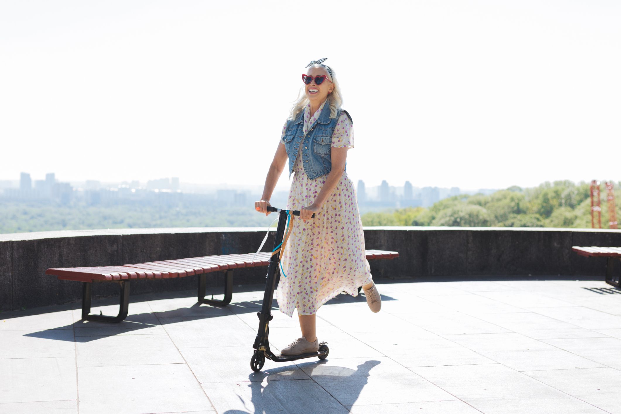 An older woman uses a Bird-like scooter on a sidewalk.