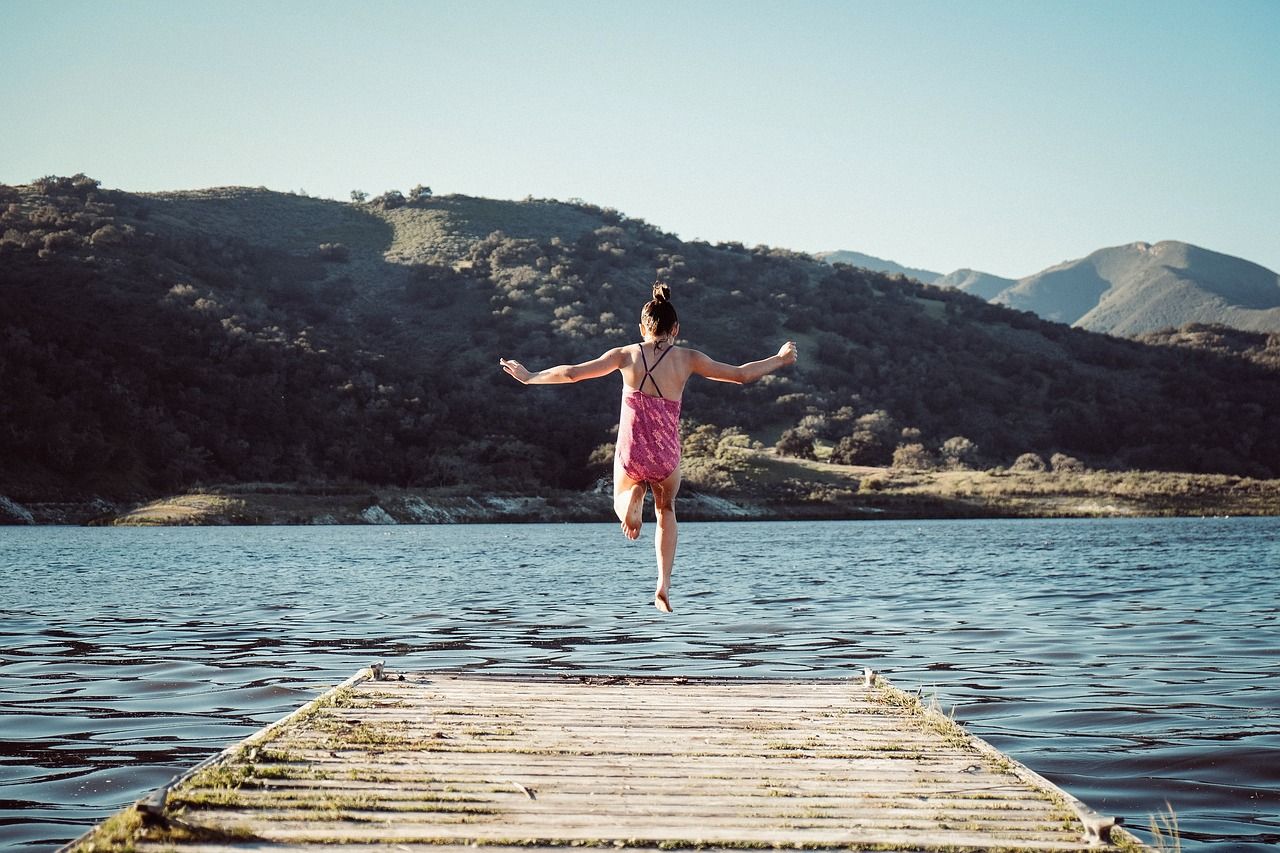 A young girl jumps off the end of a dock into a lake.