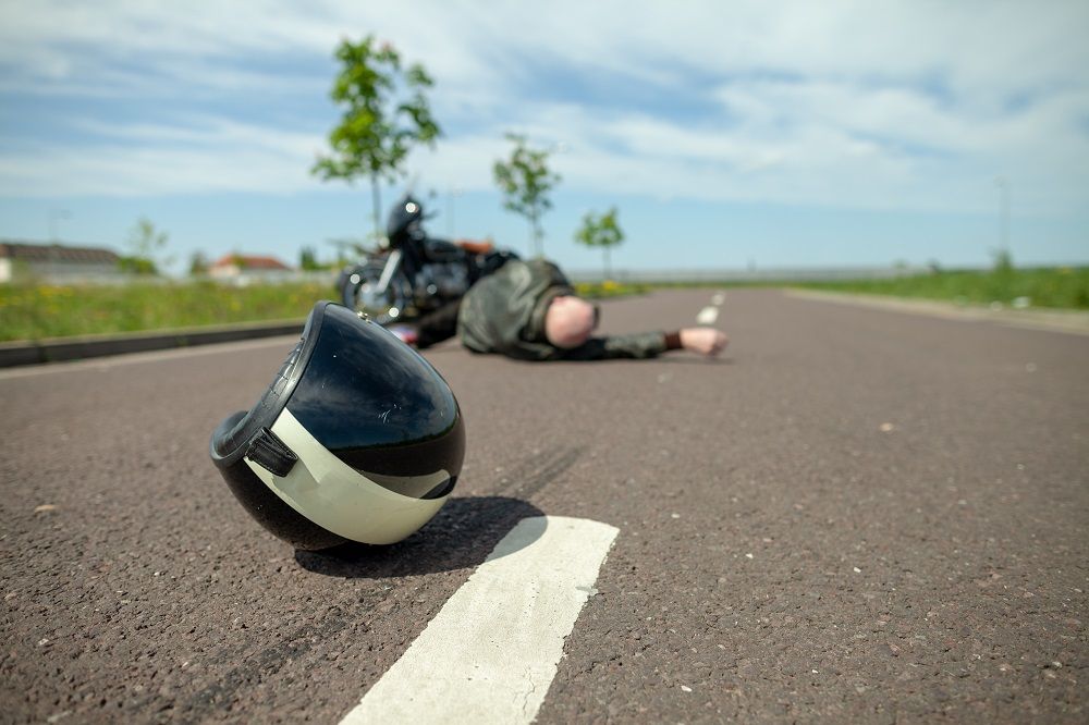 Man Lying on Ground Next to Motorcycle and Helmet