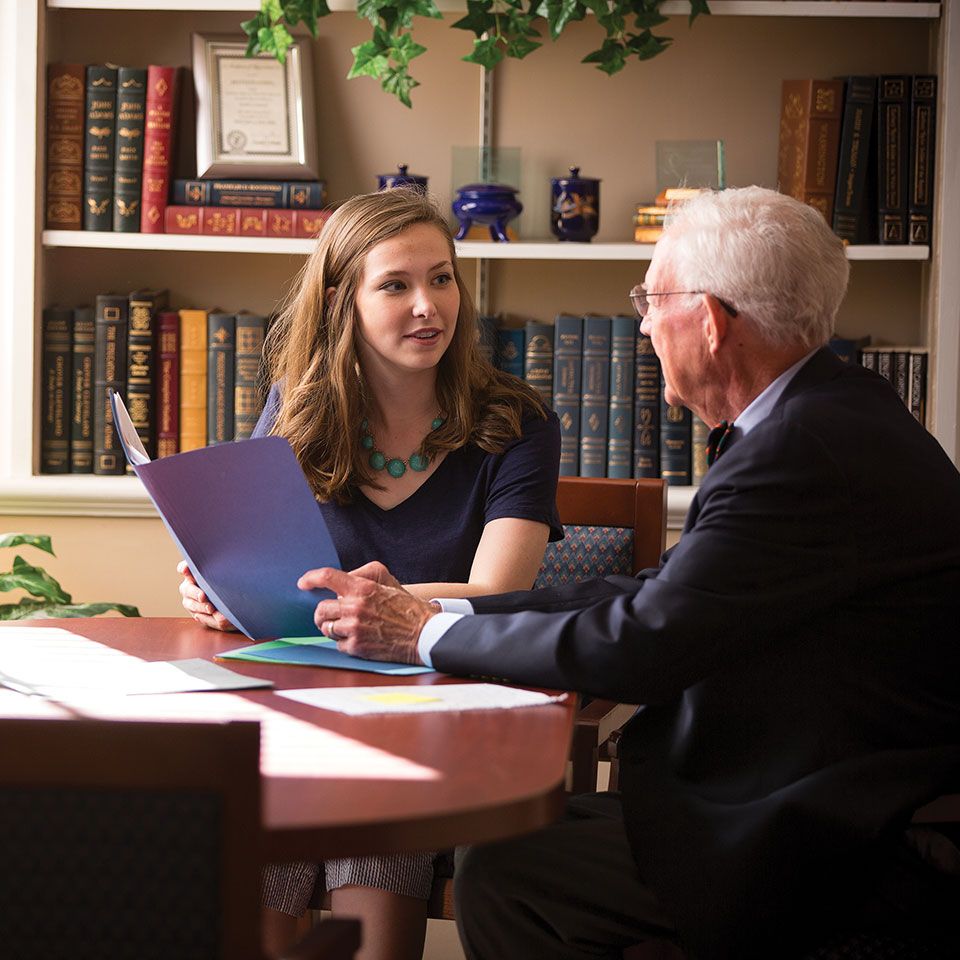 Berry alumna Ree Palmer sits at a table with her mentor in front of a bookshelf.