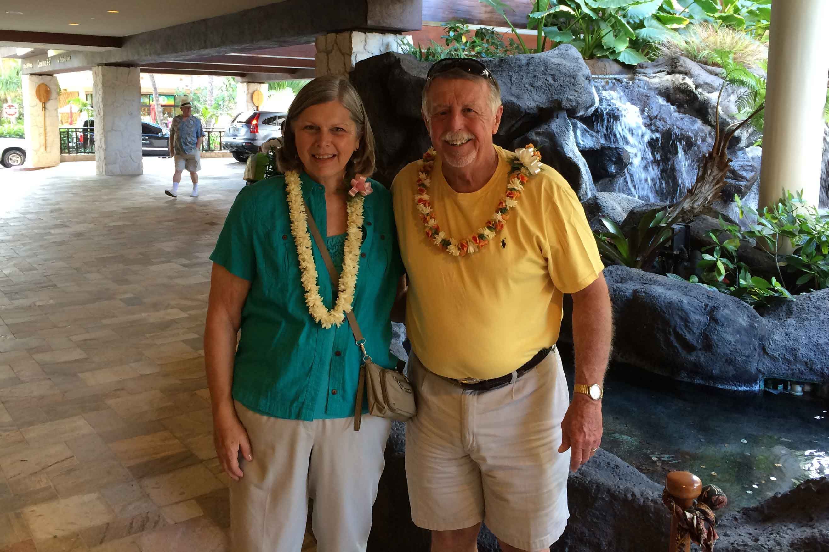 Berry alumni couple wear leis in front of a pond and rocks