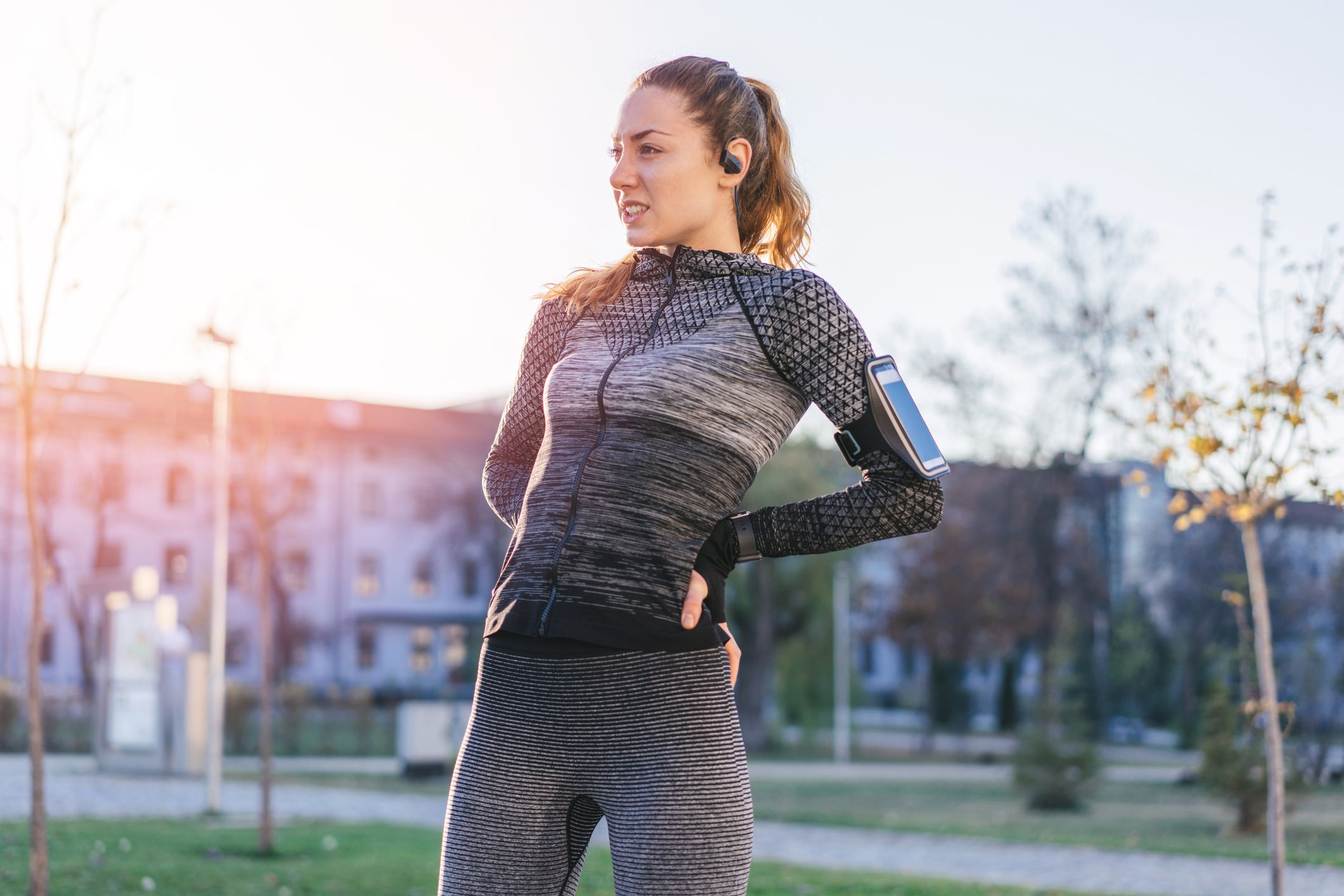 A runner grimaces and places her hands on her lower back while stretching.