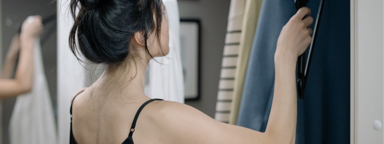 a woman in a black tank top looking at sweater hanging in a closet
