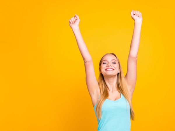 blonde woman in light blue tank top raising her arms for aesthetic procedure
